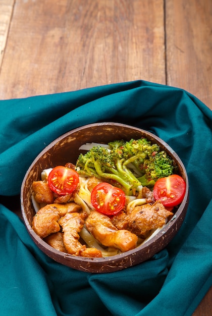 Udon di pollo in salsa giapponese su un piatto di gusci di cocco su un tovagliolo blu. Foto verticale