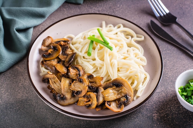 Udon noodles fritti funghi prataioli e verdi su un piatto sul tavolo