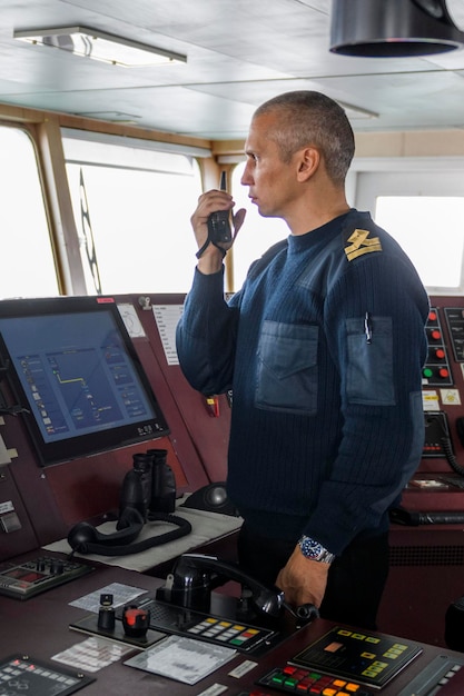 Ufficiale di guardia con radio sul ponte di navigazione Uomo caucasico in maglione uniforme blu sul ponte della nave da carico