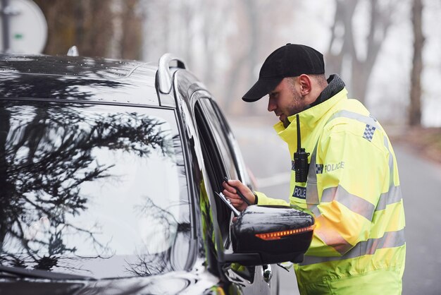 Ufficiale di polizia maschio in uniforme verde che controlla il veicolo sulla strada.