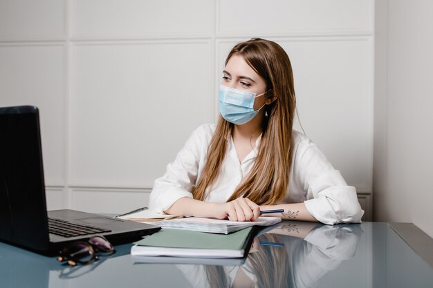 Ufficio della donna a casa con la maschera d'uso del computer portatile e studiare online