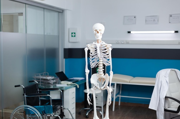 Ufficio medico vuoto con scheletro del corpo umano utilizzato come strumenti professionali durante l'esame dell'osteopatia. Vista frontale del modello anatomico in piedi nella stanza d'ospedale senza nessuno al suo interno. Concetto di medicina