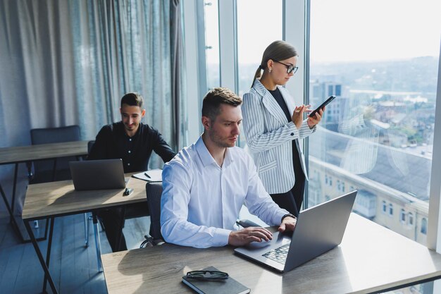 Ufficio moderno Giovane team di uomini d'affari in abiti formali che discutono dei dettagli del progetto e guardano lo schermo del laptop mentre collaborano durante la riunione nella moderna sala del consiglio