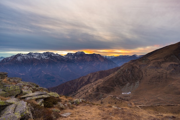 Ultima luce solare sulla valle alpina con vette luminose e nuvole panoramiche