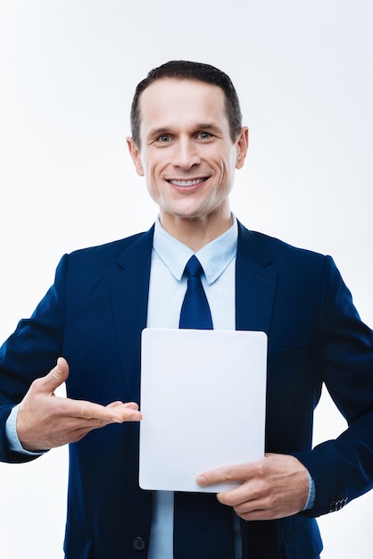 Ultima tecnologia. Uomo d'affari felice bello felice che indica al tablet e sorridente mentre lo si utilizza per il lavoro