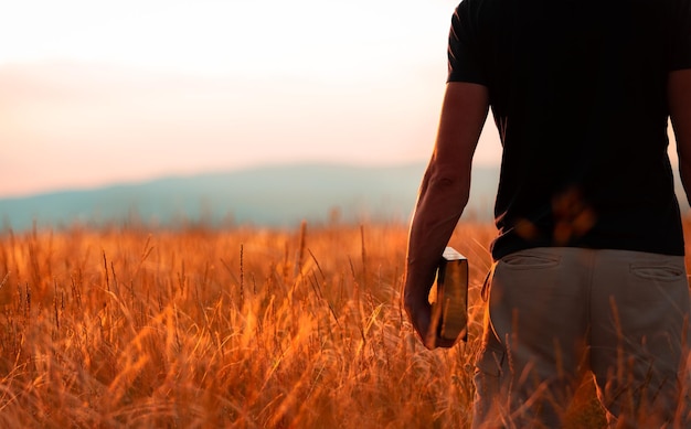 Umano che prega sulla santa Bibbia in un campo durante un bellissimo tramonto.