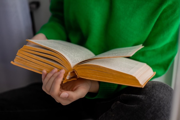 Umano in jeans e un maglione verde tiene in mano un libro aperto. avvicinamento. Foto di alta qualità