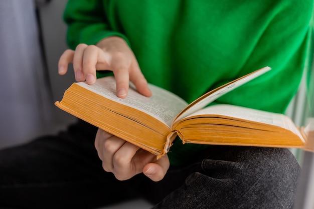 Umano in jeans e un maglione verde tiene in mano un libro aperto. avvicinamento. Foto di alta qualità