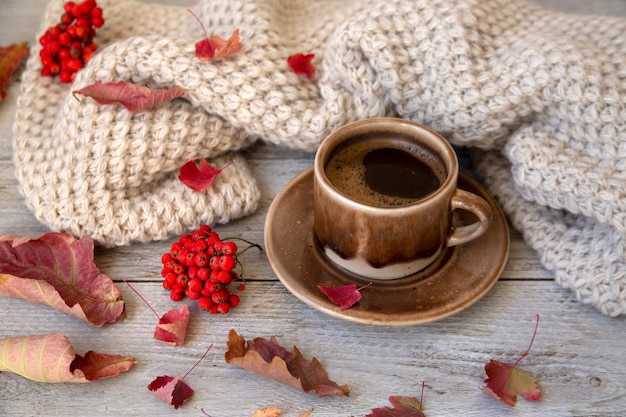 Umore autunnale sfondo autunnale Tazza di caffè sciarpa lavorata a maglia foglie autunnali e bacche su uno sfondo di legno