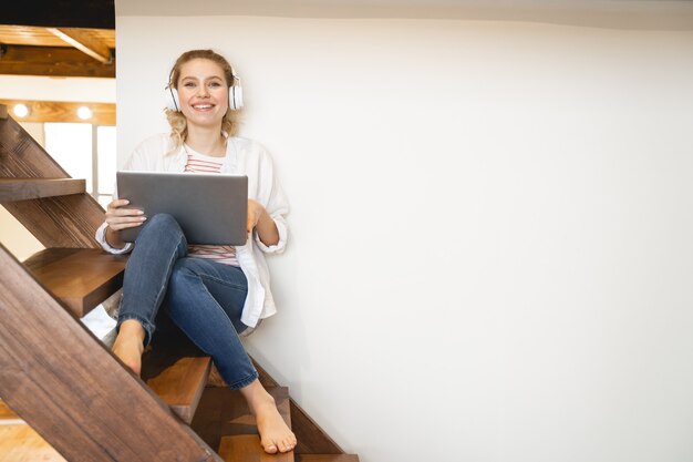 Umore gioioso. Una ragazza bionda contenta che continua a sorridere mentre lavora al suo progetto