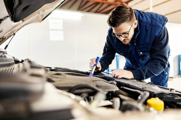 Un addetto al servizio auto che controlla il motore sotto il cofano dell'auto in garage