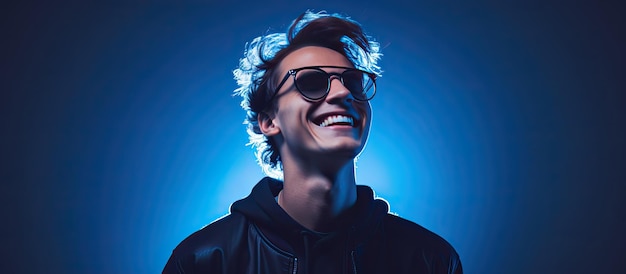 Un adolescente alla moda che indossa una manica lunga nera e occhiali si pone con un sorriso su uno sfondo blu illuminato da luci al neon che rappresentano un ciao