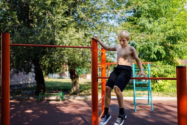 Un adolescente atletico si siede sulla barra trasversale aggrappato alla ringhiera Street workout su una barra orizzontale nel parco della scuola