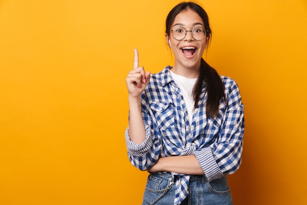 un'adolescente carina sorpresa emotiva felice con gli occhiali in posa isolata sul muro giallo ha un'idea.
