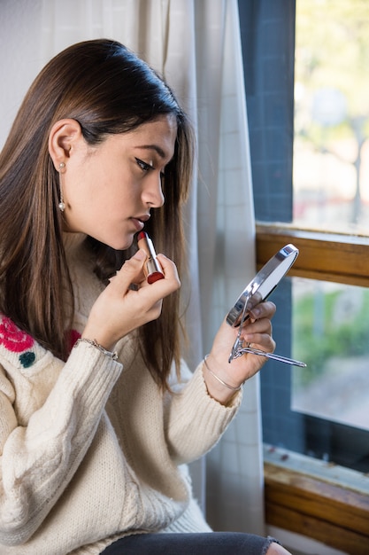 Un adolescente che applica un rossetto con uno specchio in mano