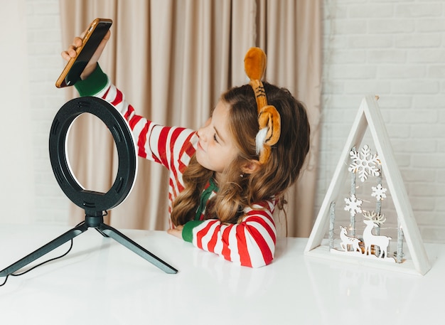 Un'adolescente che scrive sul blog del Natale. bambino blogger in pigiama a righe registra video al telefono.