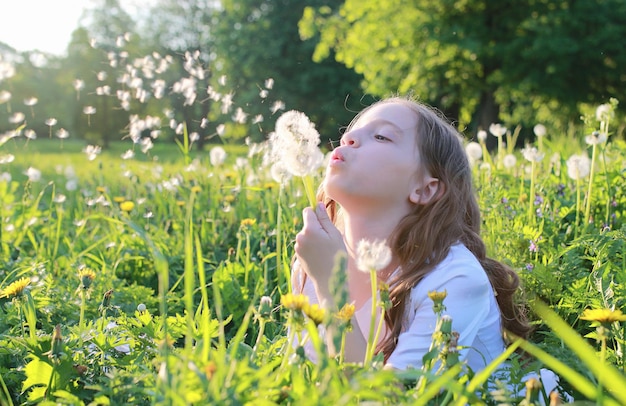 Un adolescente che soffia i semi da un fiore di dente di leone in un parco primaverile