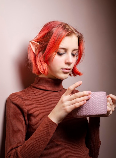 Un'adolescente con i capelli rosa beve il tè da una tazza grande