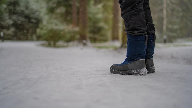 Un adolescente con stivali blu invernali si erge sulla neve bianca su un sentiero lusinghiero.