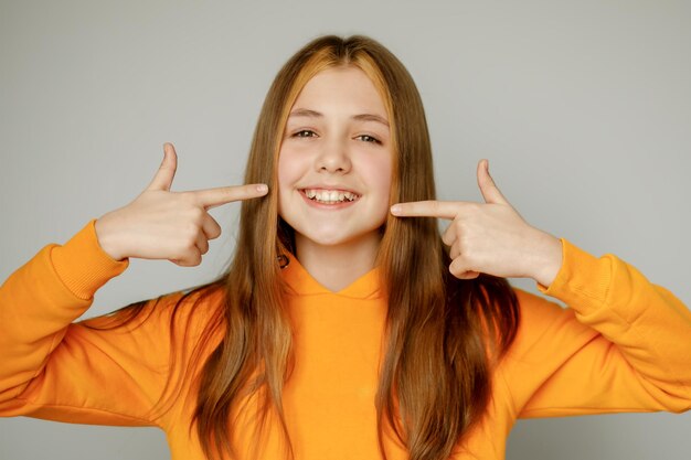 Un'adolescente in abiti arancioni sorride e mostra i suoi denti frastagliati con le sue manimedicina dentale
