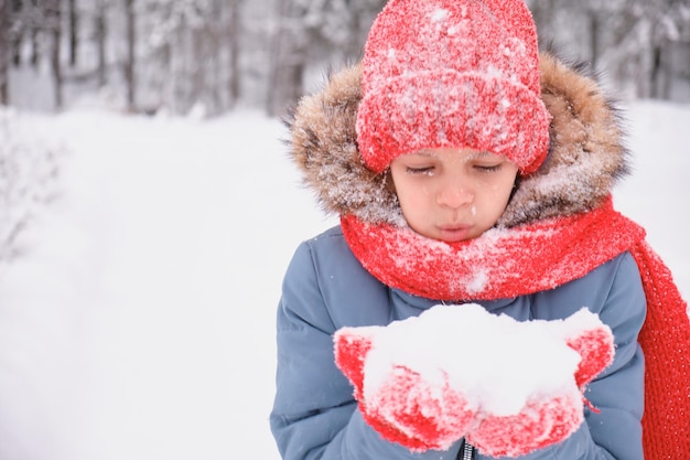 Un'adolescente soffia sulla neve tra i palmi delle mani e sventola guanti e un cappello lavorato a maglia che cambia il tempo