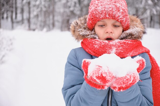 Un'adolescente soffia sulla neve tra i palmi delle mani e sventola guanti e un cappello lavorato a maglia che cambia il tempo