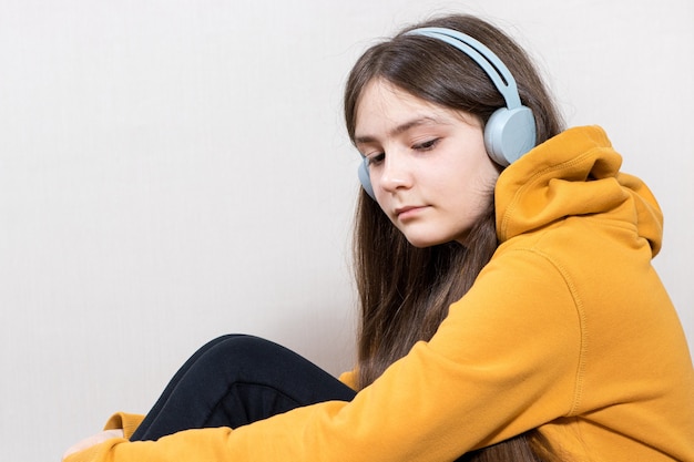 Un'adolescente triste si siede in felpa con le cuffie su uno sfondo bianco