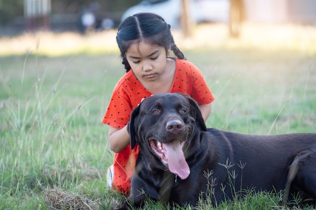 Un'adorabile bambina del sud-est asiatico in abiti rossi gioca con il suo grosso cane nel cortile sul retro o sul davanti la sera. Concetto di amante degli animali