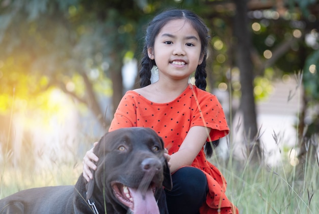 Un'adorabile bambina del sud-est asiatico in abiti rossi gioca con il suo grosso cane nel cortile sul retro o sul davanti la sera. Concetto di amante degli animali