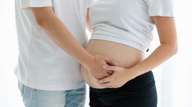 Un'adorabile giovane coppia asiatica, marito e moglie, che stanno insieme sorridendo e toccando la pancia di una donna incinta con amore e cura. Concetto di famiglia felice e sano.