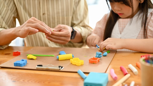 Un'adorabile giovane ragazza asiatica che scolpisce l'argilla colorata per modellare l'argilla con il suo papà ritagliata l'immagine