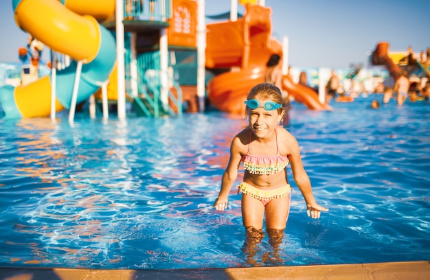 Un'adorabile ragazza con gli occhiali blu per nuotare e un costume da bagno luminoso si trova in una piscina con acqua limpida vicino al lato