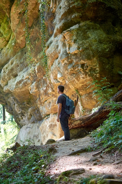 Un adulto zaino in spalla che cammina intorno a una grotta in una foresta in una giornata di sole