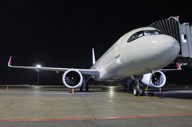 Un aereo a reazione bianco per passeggeri si trova presso il ponte aereo collegato a un alimentatore esterno su un grembiule notturno dell'aeroporto