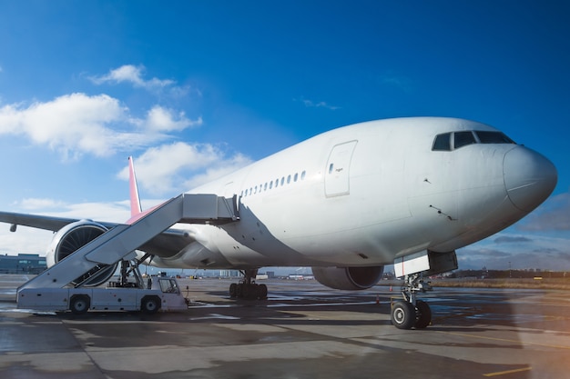 Un aereo di linea passeggeri in tutto il corpo parcheggiato all'aeroporto con una rampa all'ingresso, contro un cielo blu