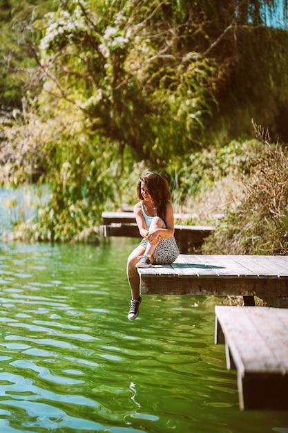 Un'affascinante giovane donna in gonna è seduta su un ponte di legno sullo sfondo della natura