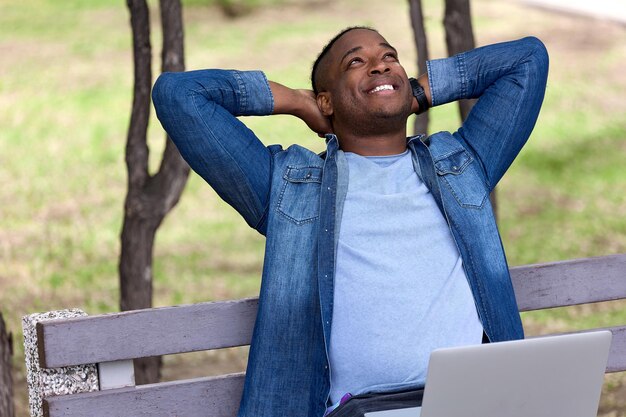 Un africano sorridente lavora all'aperto in un parco verde e alza lo sguardo pensieroso.