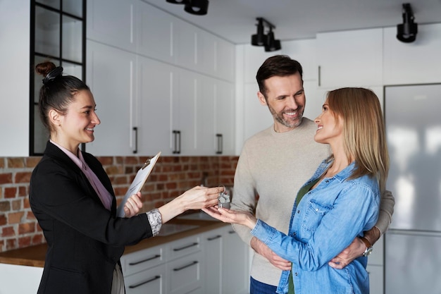 Un agente immobiliare sorridente che dà le chiavi della casa a una coppia.