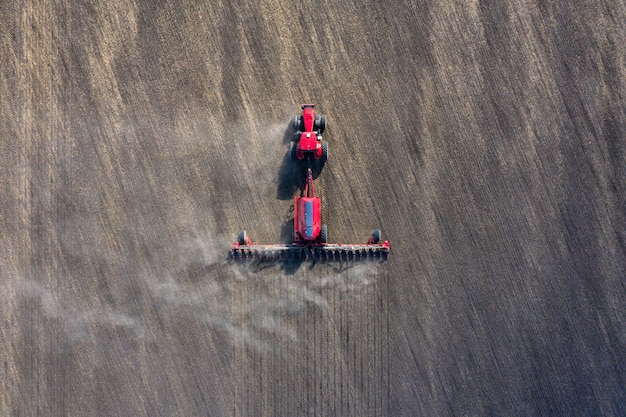 Un agricoltore in un trattore prepara il terreno con un coltivatore di semina come parte del lavoro di pre-semina all'inizio della stagione agricola primaverile su terreni agricoli.