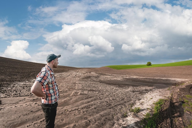 Un agronomo maschio esamina i campi dopo forti piogge sullo sfondo di nuvole piovose. Valutazione dei danni meteorologici terreni agricoli dopo l'alluvione