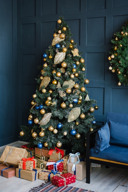 Un albero di Natale con palloncini oro e blu con doni sotto di esso si trova nel soggiorno con pareti blu