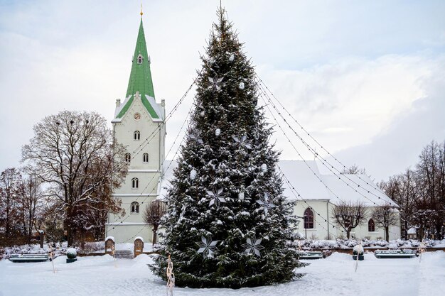 Un albero di Natale decorato in una piazza cittadina con una chiesa sullo sfondo Dobele Lettonia