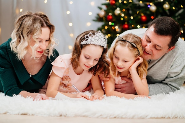 Un'allegra famiglia felice scrive una lettera a babbo natale all'albero di natale