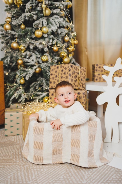 Un allegro ragazzino di 23 anni è in piedi vicino a un albero di Natale circondato da ghirlande e presenta il concetto di una fiaba di Natale una vacanza per bambini piccoli Albero di Natale