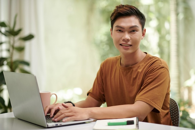 Un allegro studente asiatico di informatica che programma in un portatile a casa