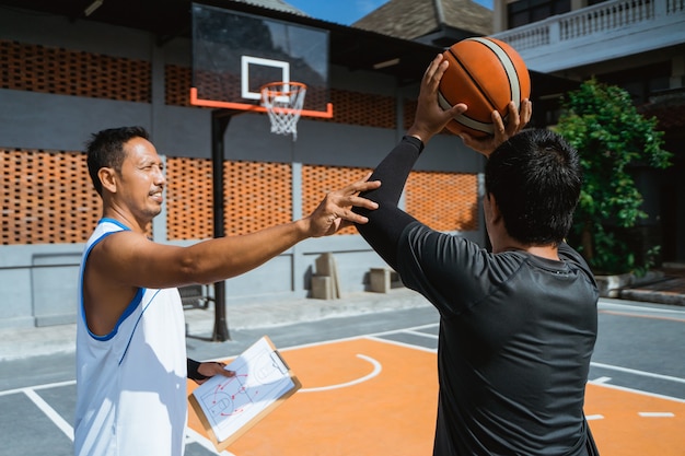 Un allenatore consiglia a un giocatore di basket maschile di tirare la palla nel canestro