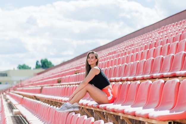 Un'allenatrice dai capelli scuri si trova sulla pista rossa dello stadio, vestita in divisa sportiva.