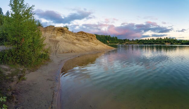 Un'alta scogliera sulla riva di un lago con nuvole colorate nel cielo al tramonto