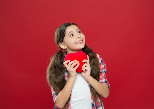 Un amore un cuore. Bambina che tiene cuore rosso. Avere problemi cardiaci e mal di cuore. Piccolo bambino che esprime amore il giorno di San Valentino. Ragazza carina innamorata. Buon San Valentino.