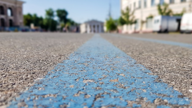 Un'ampia striscia blu su una superficie nera come l'asfalto. strada asfaltata in città, estate, alberi verdi, cielo blu. Inquadratura dal basso dalle linee blu centrali.